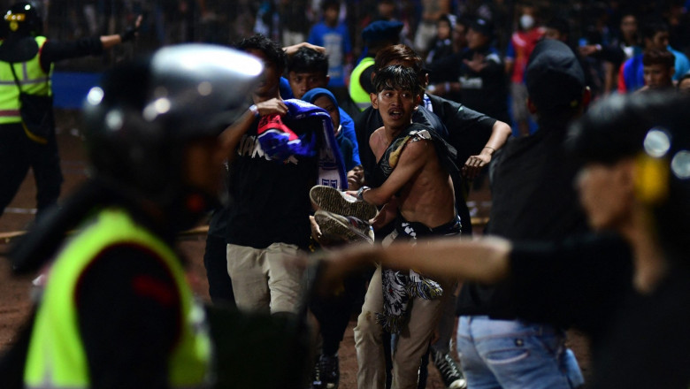 In this picture taken on October 1, 2022, a group of people carry a man at Kanjuruhan stadium in Malang, East Java