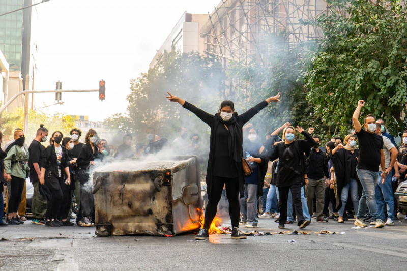 bărbat în negru cu mâini ridicate în dreptul capului în timpul protestelor din Iran