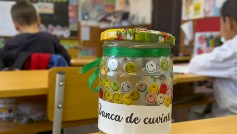 borcan cu stickere cu fete zambitoare pe care scrie „banca zambitoare” asezat pe o banca intr-o clasă