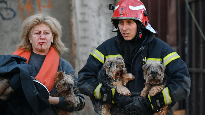 An emergency worker carries dogs as he escorts a local resident outside a partially destroyed multistorey office building after several Russian strikes hit the Ukrainian capital of Kyiv on October 10, 2022