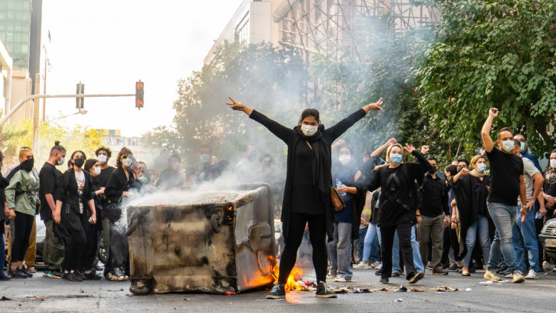 Protestatari pe o stradă din Teheran cu un tomberon în flăcări
