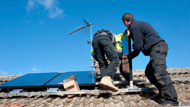 Doi oameni montează panouri fotovoltaice pe un acoperiș.