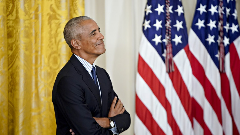 Barack Obama cu mâinile încrucișate lângă steagul SUA