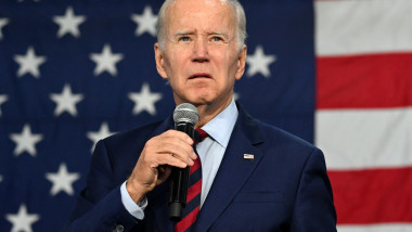 Joe Biden vorbește la microfon cu un steag american în spate
