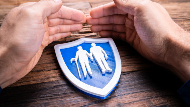 mâini împreunate în jurul unei sigle care arată doi pensionari, simbolizează protecție și sprijin la pensie