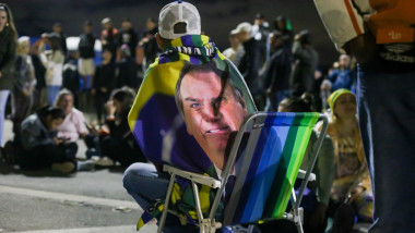 protestatar stă pe un scaun pliant cu steag pe spate care are chipul lui Bolsonaro