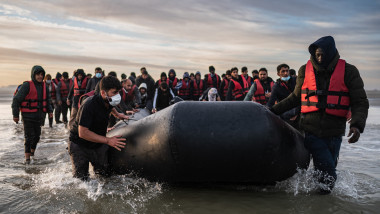 migranți pun o barcă neagră la apă
