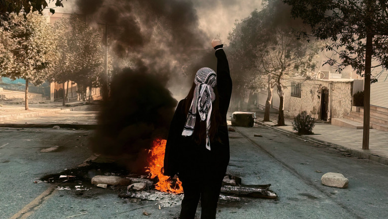 protestatara cu pumnul ridicat în fața unor resturi în flăcări
