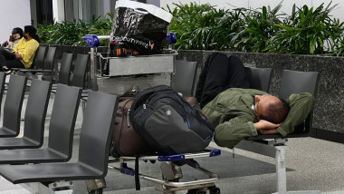 barbat care doarme pe scaune in aeroport cu bagajele langa el