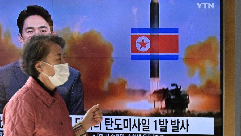 o femeie trece pe langa un ecran tv cu stirea despre racheta lansata de coreea de nord