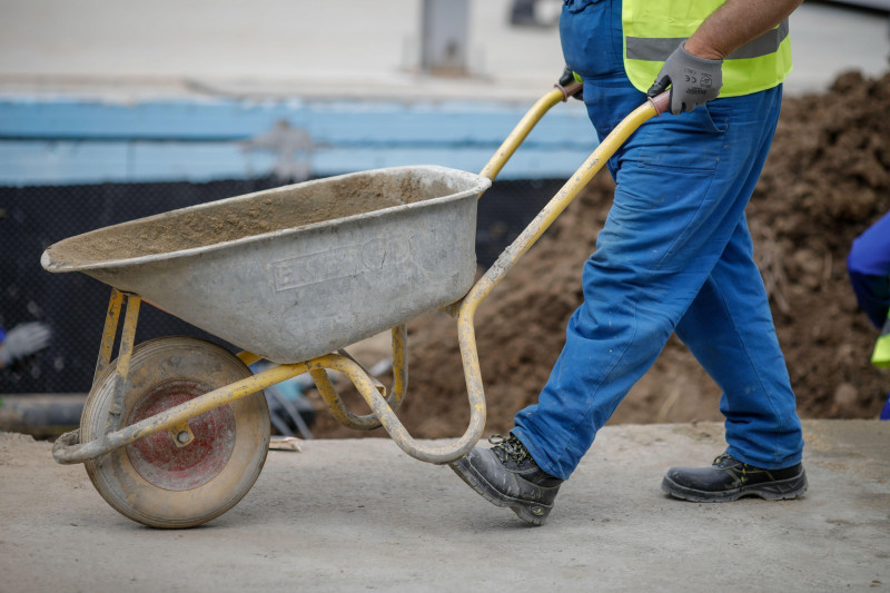 Bucharest, Romania - May 8, 2020: Details with a construction worker pushing a wheelbarrow on a construction site.