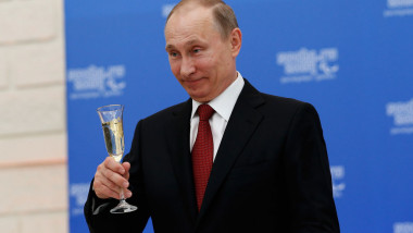 Vladimir Putin zâmbește în timp ce ține un pahar de șampanie