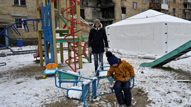 copil ucraina se joaca intr-un loc de joaca langa un bloc bombardat