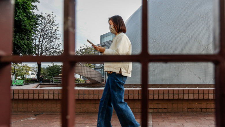 Femeie cu un telefon merge pe stradă, văzută printr-o fereastră cu grilaj