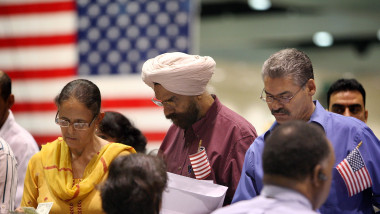 Femeie îmbrăcată în galben, bărbat turban și bărbă și bărbat cu mustață, cu steagul SUA în spate