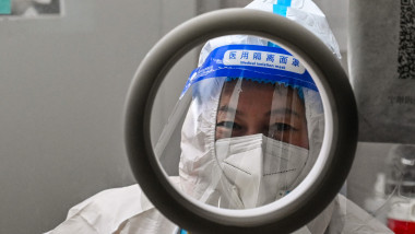 fața unei lucrătoare sanitare chineze cu vizieră și costum de siguranță sub o lupă