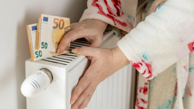 O femeie atinge caloriferul și ține în mână o bancnotă de 50 de euro