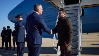 Zelenski dă mâna cu un oficial american în fața scării unui avion oficial