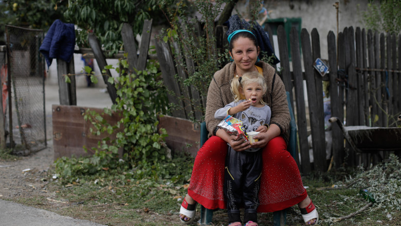 femeie roma cu copil in brate stau la poarta intr-un sat in romania