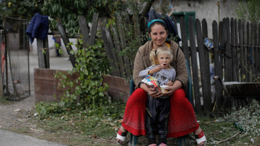 femeie roma cu copil in brate stau la poarta intr-un sat in romania
