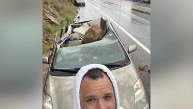 un barbat isi face selfie in fata unei masini distruse de un bolovan