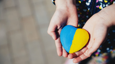 Un copil mic ține o piatră în formă de inimă cu steagul Ucrainei