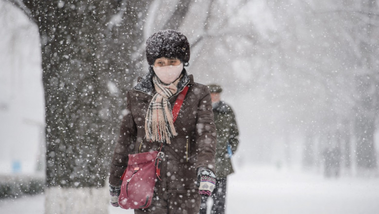 femeie îmbrăcată gros merge prin ninsoare