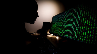 Un hacker in fața unui ecran de computer care afișează coduri binare.
