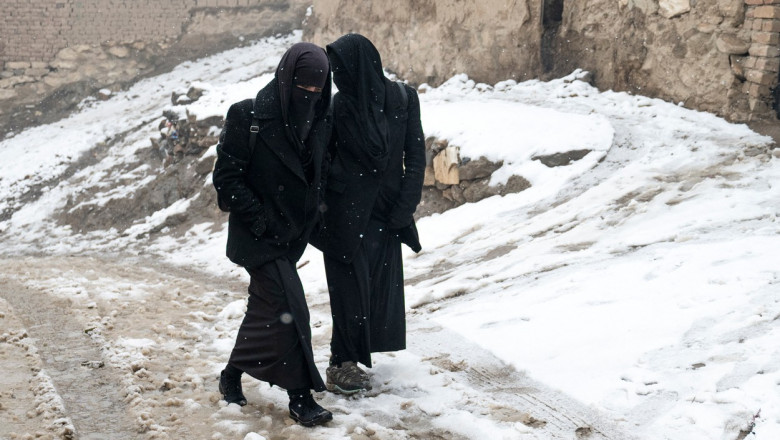 Două femei afgane merg pe un drum înzăpezit.