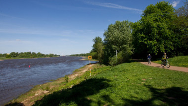 O persoană merge pe bicicletă pe o pista din apropierea unui râu.
