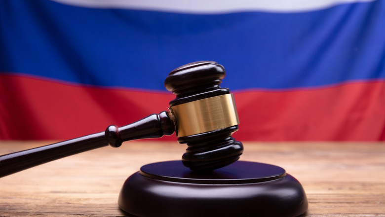 Un ciocan de judecator în prim plan, cu un steag al Rusiei pe fundal.