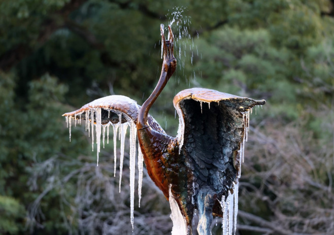 A frozen crane sculpture fountain hangs icicles from its wings