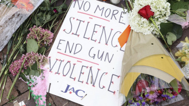 carton inscripționat cu un mesaj împotriva violenței cu arme de foc lângă buchete de flori