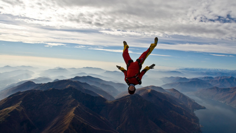 This skydiver is jumping out of a plane in a head down position. The sun behind the diver is perfect in between the beautiful mountain scenery. Below the jumper the cloud base is sitting because it is very cold at this time a year in this area