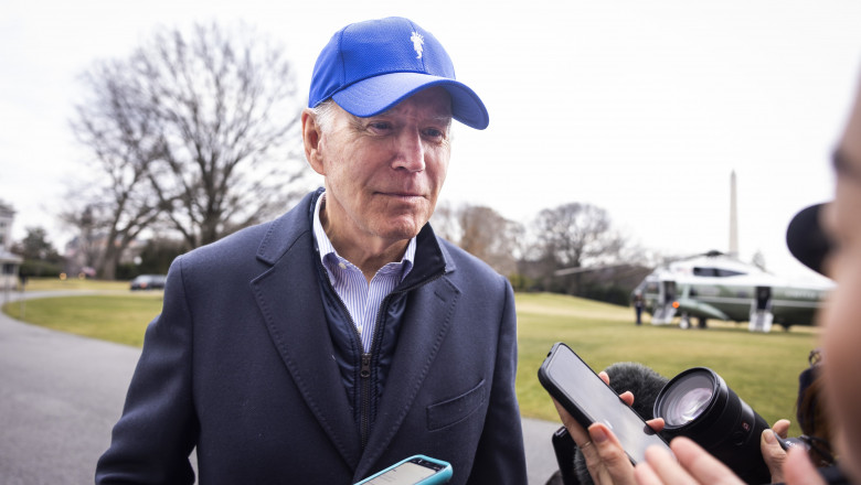 Joe Biden cu șapcă albastră în fața reporterilor cu telefoane și microfoane