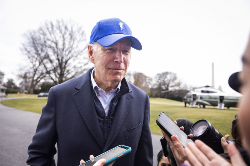 Joe Biden cu șapcă albastră în fața reporterilor cu telefoane și microfoane