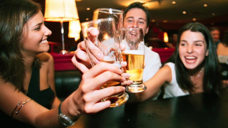 două femei și un bărbat ciocnesc paharele cu bere într-un bar