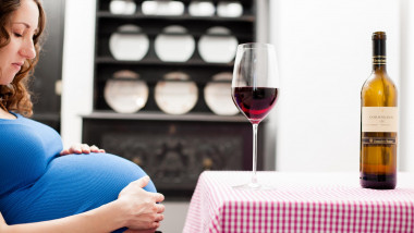 femeie gravidă la masă cu un pahar de vin