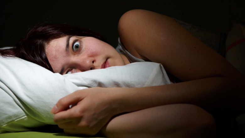 O femeie întinsă în pat are ochii puternic deschişi de parcă tocmai s-a trezit din somn.