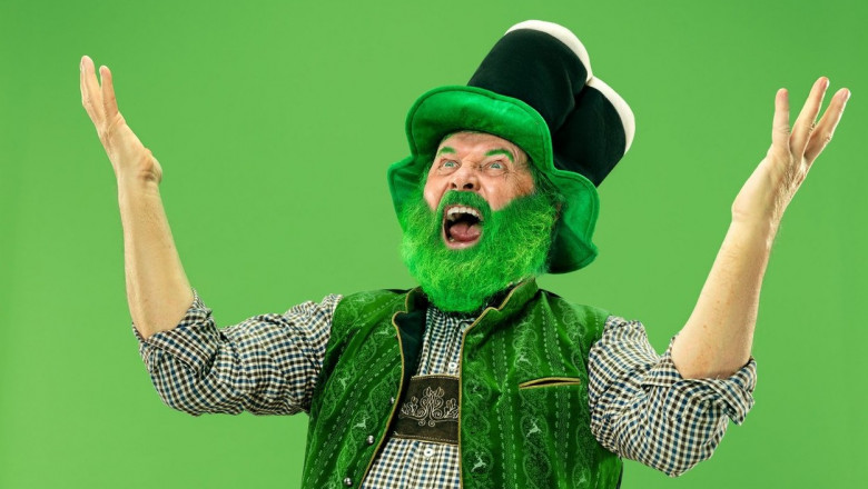 A smiling surprised happy senior man in a leprechaun hat with beard at green studio