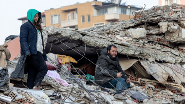 O femeie și un bărbat stau pe un morman de resturi ale unei clădiri prăbușite la cutremur în orașul Antakya, pe 12 februarie 2023,