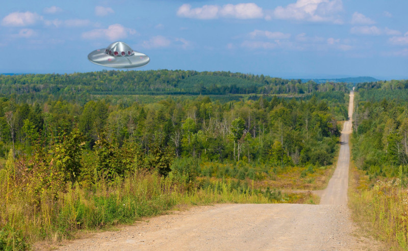 UFO over a thick forest in Maine next to a long road