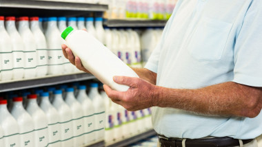 Un bărbat se uită la o sticlă de lapte în faţa unui raft de produse lactate dintr-un magazin.