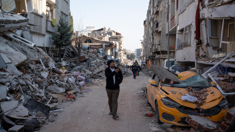 Un bărbat face fotografii cu telefonul în timp ce se plimbă printre două rânduri de blocuri avariate de cutremur în Turcia, provincia Hatay.