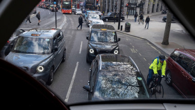 Pedestrians cross the road and a cyclist passes cars and taxies which stretch into the distance, seen from the top deck of a London bus in Aldwych, on 13th April 2022, in London, England.
