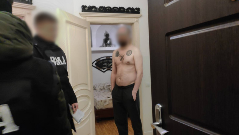 bărbat în pielea goală cu trei tatuaje deasupra pieptului și doi polițiști în echipament special