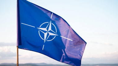 Un steag cu sigla NATO flutură în vânt.