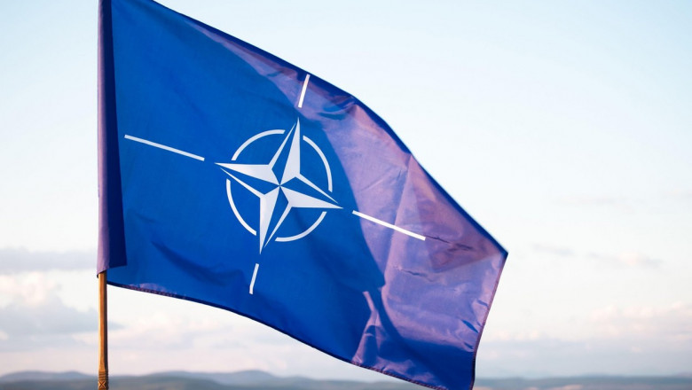 Un steag cu sigla NATO flutură în vânt.