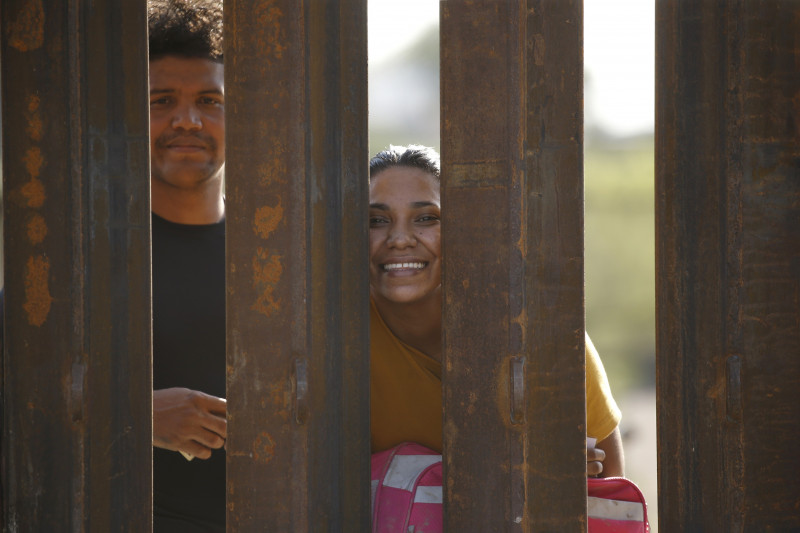 Migranți privesc prin gardul de la granița SUA cu Mexicul