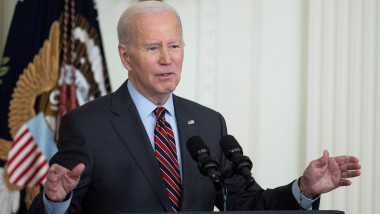 Joe Biden la pupitrul prezidențial gesticulează cu ambele mâini ridicate